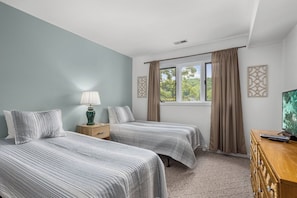 A room with two beds, a nightstand with a lamp, a TV, and a window with curtains.