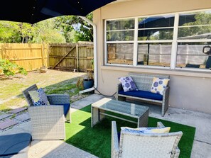 An outdoor patio with wicker furniture, a glass table, and a view of a wooden fence and trees.