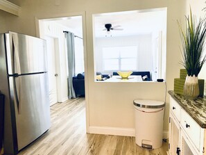 A kitchen with a stainless steel refrigerator, a white trash bin, and a dining area with a table and chairs.