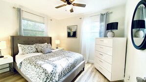 A bedroom with a bed, a nightstand, a dresser, a ceiling fan, and a window with curtains.