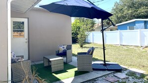 A patio area with wicker furniture, a blue umbrella, and a small artificial lawn.