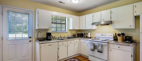 A compact kitchen with white cabinets, a stove, microwave, and a coffee maker.