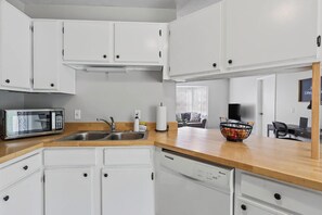 A modern kitchen with white cabinets, a stainless steel sink, a microwave, and a dishwasher.