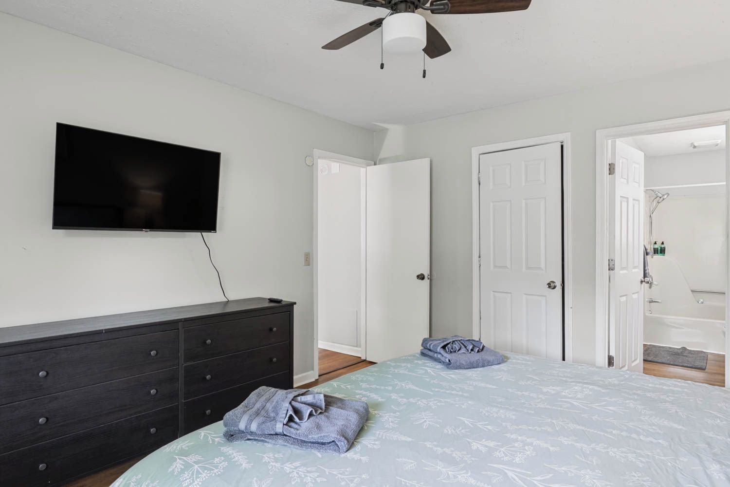A bedroom with a bed, a dresser, a television, and a ceiling fan.