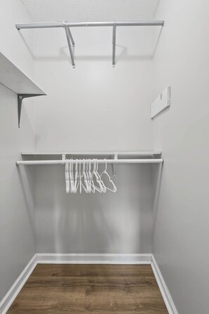A room with a wooden floor, a white ceiling, and a metal rack with clothes hanging. - Spacious 2BR Ideal for Long-Term Business Stays (Calhoun)