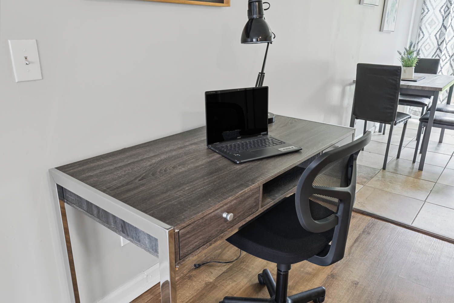 A modern office space with a dark wood desk, a laptop, a black office chair, and a desk lamp.