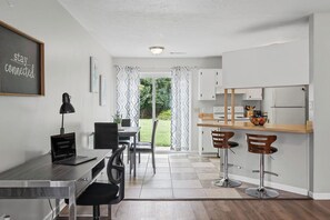A modern kitchen with a dining area, a laptop on the desk, and a sign on the wall. - Spacious 2BR Ideal for Long-Term Business Stays (Calhoun)