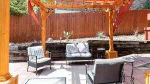 Eine Terrasse im Freien mit Korbmöbeln, einer Holz-Pergola und einem Holzzaun im Hintergrund.