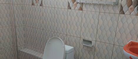 A bathroom with a white toilet, a sink with an orange basin, and patterned tiles on the walls and floor.