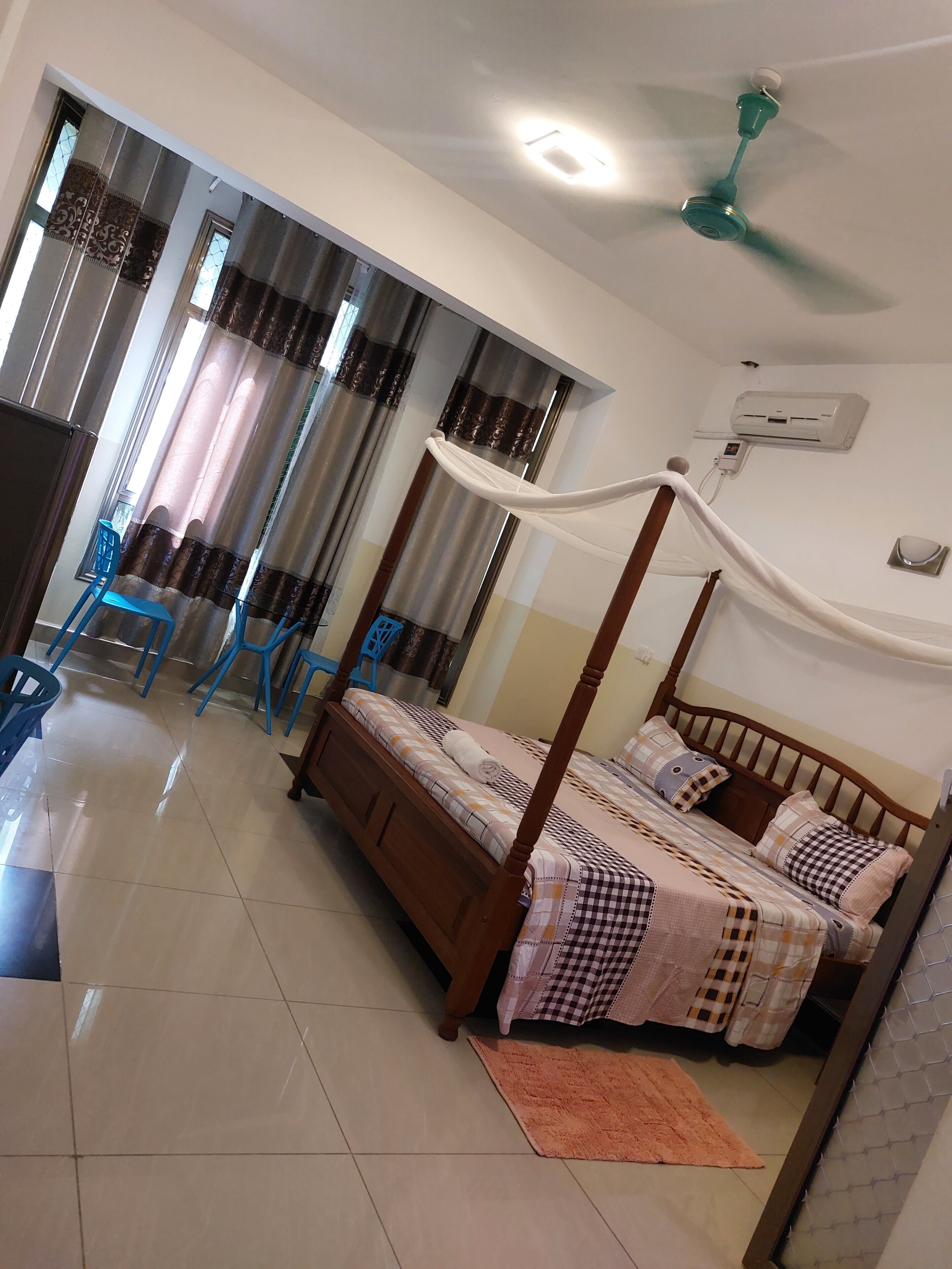 A bedroom with a four-poster bed, a ceiling fan, and a wall-mounted air conditioner.