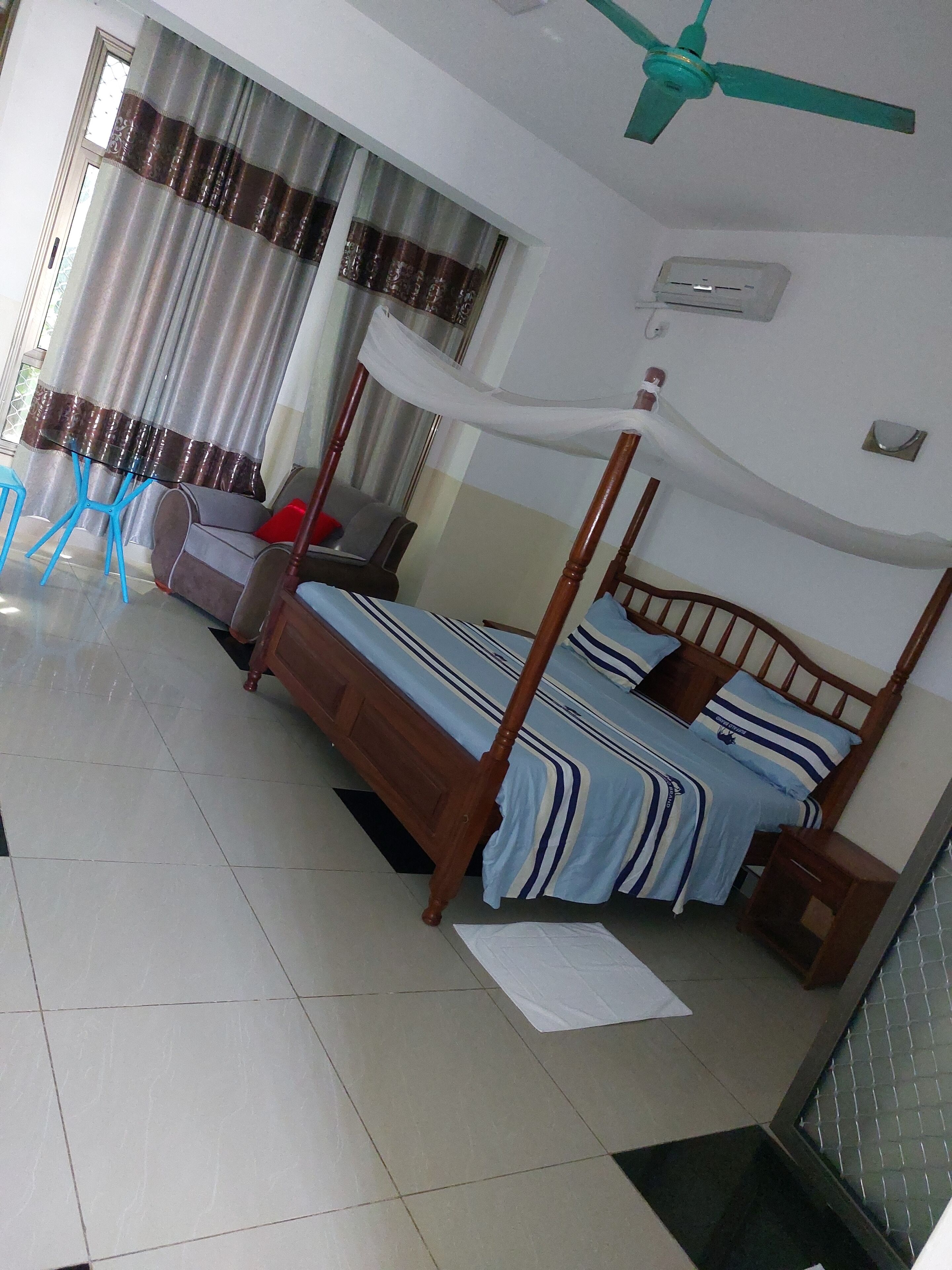 A bedroom with a four-poster bed, a ceiling fan, and a window with curtains.
