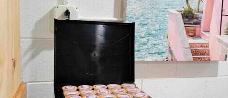 A black espresso machine with the brand name PRIMO, placed on a wooden floor next to a white wall.