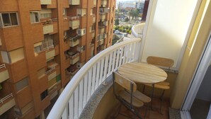 Een balkon met een kleine tafel en twee stoelen, met uitzicht op een woongebied met bakstenen gebouwen.