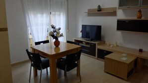 Een ruimtelijke woonruimte met een eettafel, stoelen, een televisie en een kitchenette.