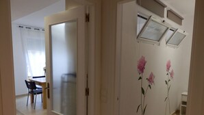 Een gang met een deur naar een kamer, een eetgedeelte met een tafel en stoelen, en een wand met bloemenbehang.
