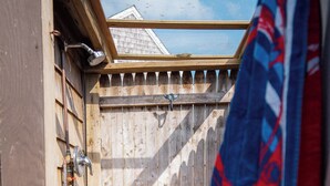 A wooden deck with a wooden fence, a metal gate, and a blue and red jacket hanging on the fence. - Steps to a private beach in a classic Cape cottage. Pet-friendly! (Dennis)
