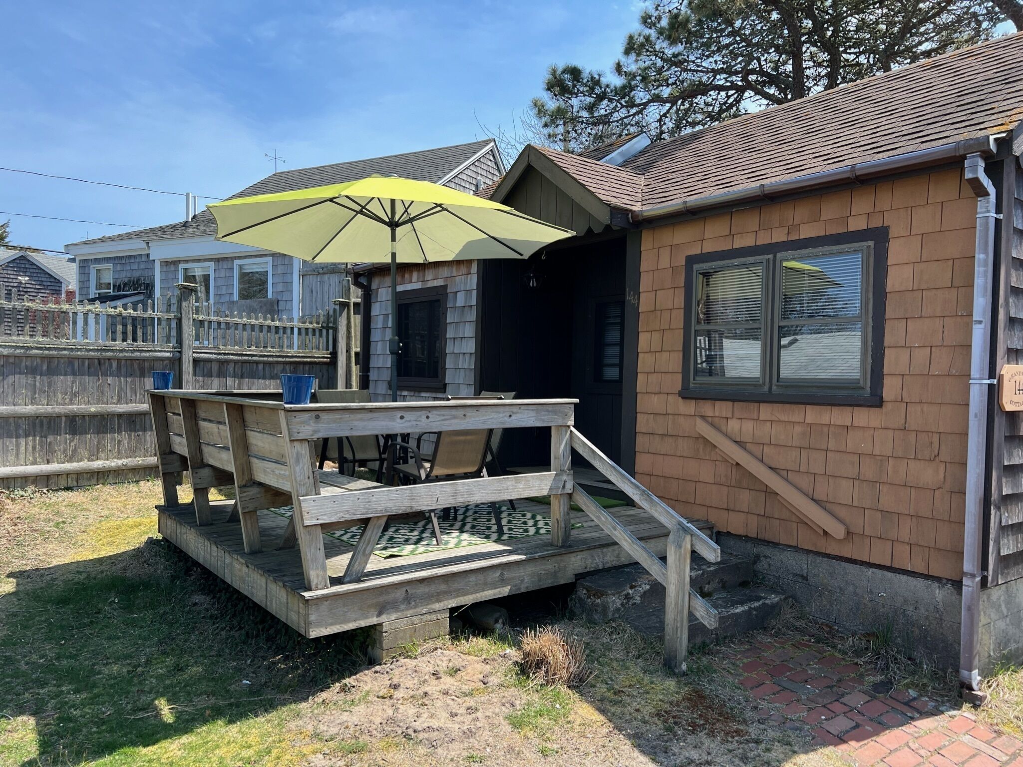 A wooden deck with a table and chairs, an umbrella, and a brick house with a window.