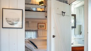 A room with a bunk bed, a wooden ceiling, a framed picture on the wall, and a bathroom visible through an open door. - Steps to a private beach in a classic Cape cottage. Pet-friendly! (Dennis)