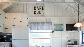 A cozy kitchen with a white refrigerator, wooden cabinets, a ceiling fan, and a window with curtains. - Steps to a private beach in a classic Cape cottage. Pet-friendly! (Dennis)