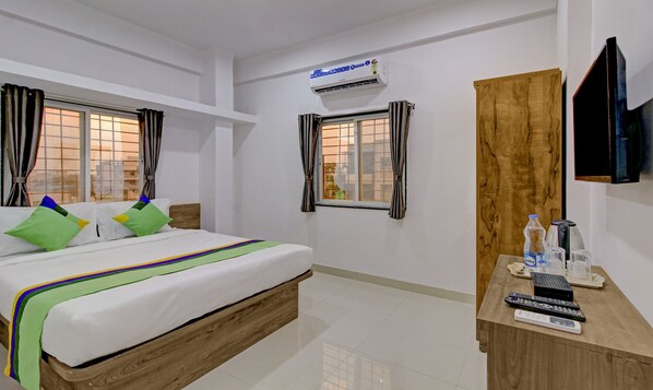 A hotel room with a bed, a wooden wardrobe, a TV mounted on the wall, and a window with curtains. - Treebo White House (Pune)