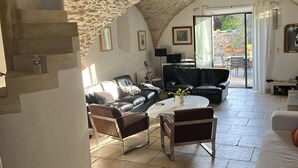 A spacious living area with a stone ceiling, a black leather sofa, a white coffee table, and a white armchair. - Maison DE Hameau - 4 KM Roussillon - 8 KM Gordes (Saint-Saturnin-lès-Apt)