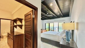A hotel room with a bed, a desk, a chair, and a view of the sea.