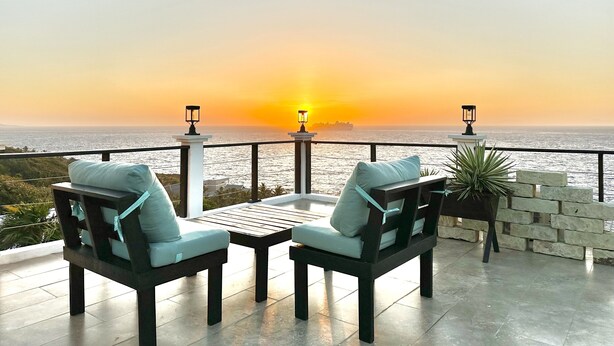 A terrace with two chairs and a table, overlooking the sea during sunset.