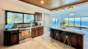 A modern kitchen with a large island, wooden cabinets, and a view of the ocean.