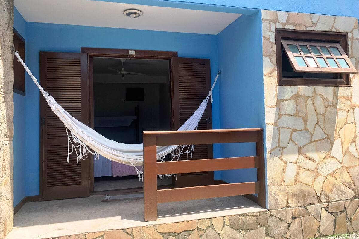 A room with a hammock, wooden shutters, and a stone wall.