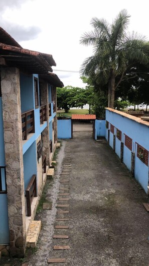 A pathway leading to a building with stone pillars and blue walls, surrounded by greenery and palm trees. - Pousada Bella Spiaggia (Paraty)