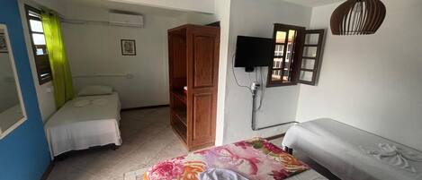 Een slaapkamer met een bed, een bank, een houten kledingkast, een televisie en een wandlamp.