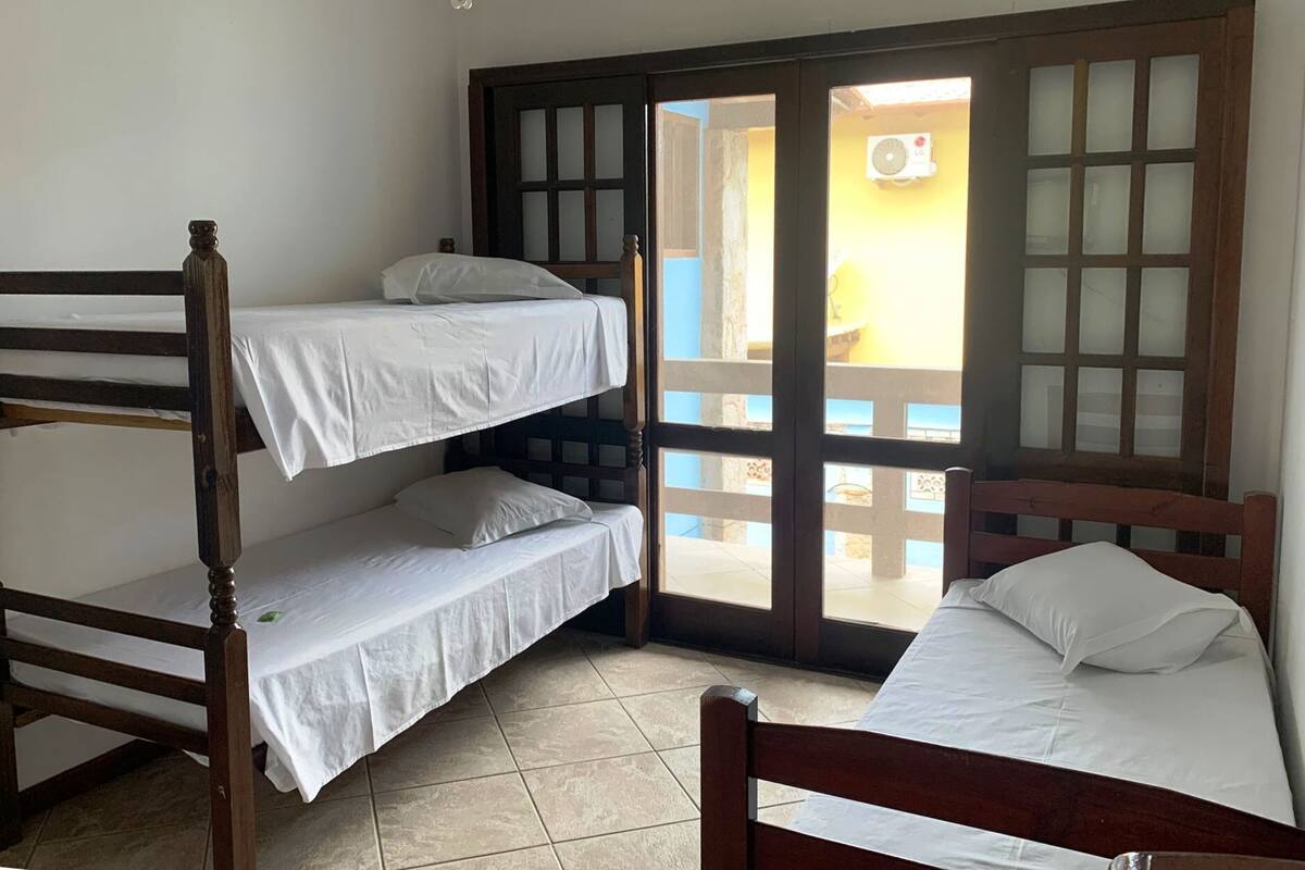 A room with a bunk bed, a single bed, and a sliding glass door leading to an outdoor area.