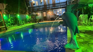 A swimming pool with a dolphin sculpture, a two-story building with outdoor seating, and a well-lit patio area. - Pousada Bella Spiaggia (Paraty)