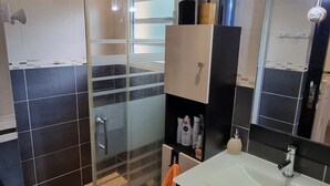 Moderni kylpyhuone, jossa on lasiseinällä varustettu suihku, allas ja peili.