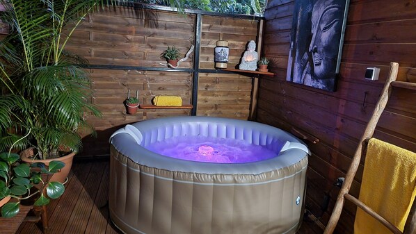 Un bain à remous dans un espace extérieur au sol en bois, agrémenté de plantes en pot et doté d’un mur en bois.