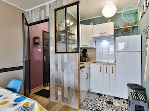 Una cocina compacta con armarios blancos, un refrigerador y una cafetera.