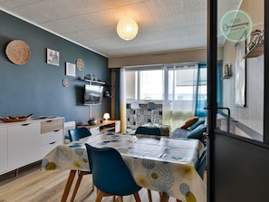 Una sala moderna con comedor, televisor y un ventanal con persianas.