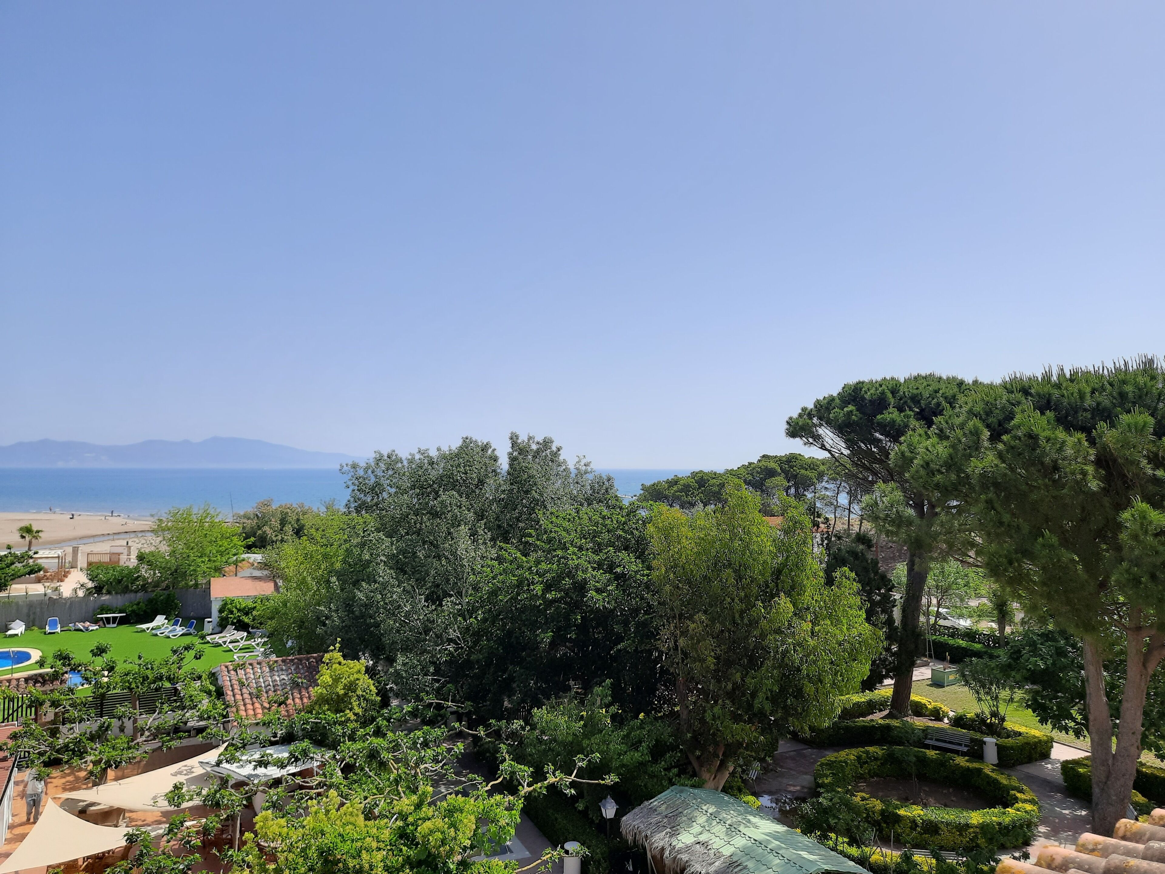 Un jardín ajardinado con piscina, sillas de descanso y vistas al mar.