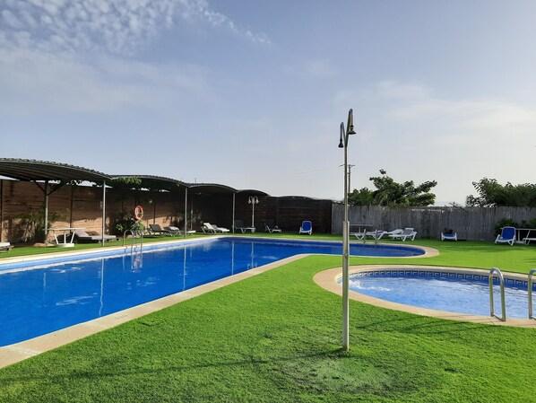 A swimming pool with a grassy area, lounge chairs, and a covered seating area. - HOTEL RIOMAR (L'Escala)