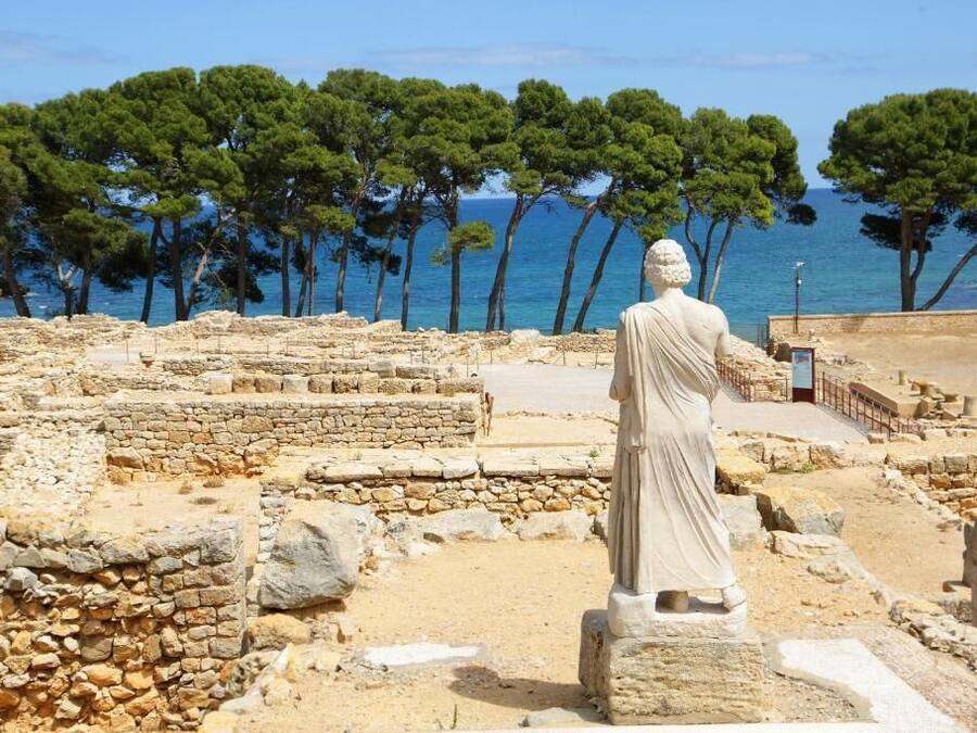 Ruinas antiguas con estructuras de piedra y una estatua clásica.