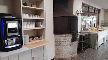 Una cocina con cafetera, estantes con tazas, un horno de piedra y una mesa para desayunar.