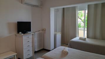 A hotel room with two beds, a TV on a dresser, a radiator, and a window with curtains.