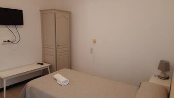 Une chambre simple, avec un lit, une petite table, un téléviseur fixé au mur et une armoire.