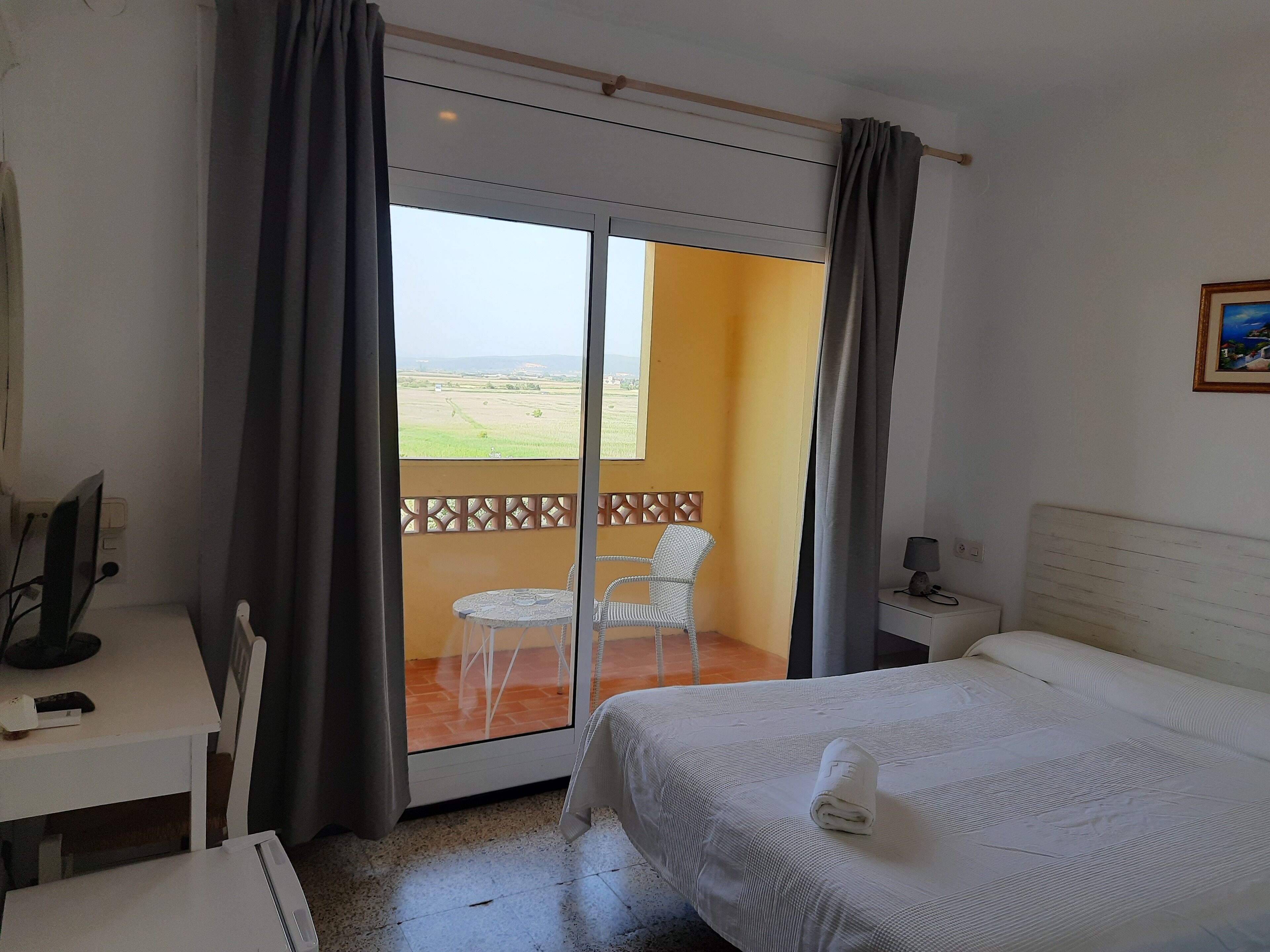 A hotel room with a bed, a desk, a chair, and a balcony with a view of the countryside.