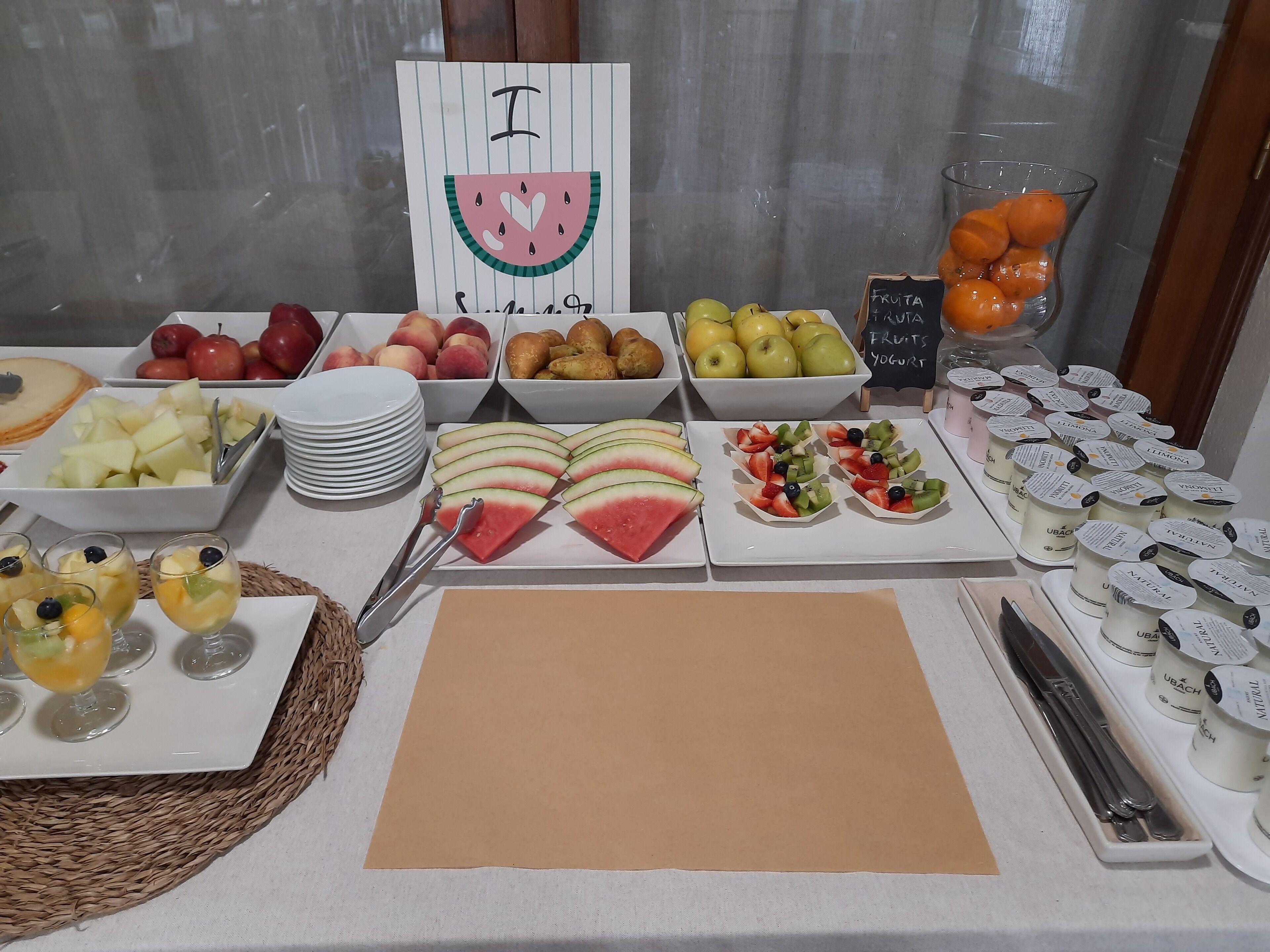 Een buffet met diverse soorten fruit, yoghurt, en een bordje met de tekst 'Ik hou van watermeloen'.