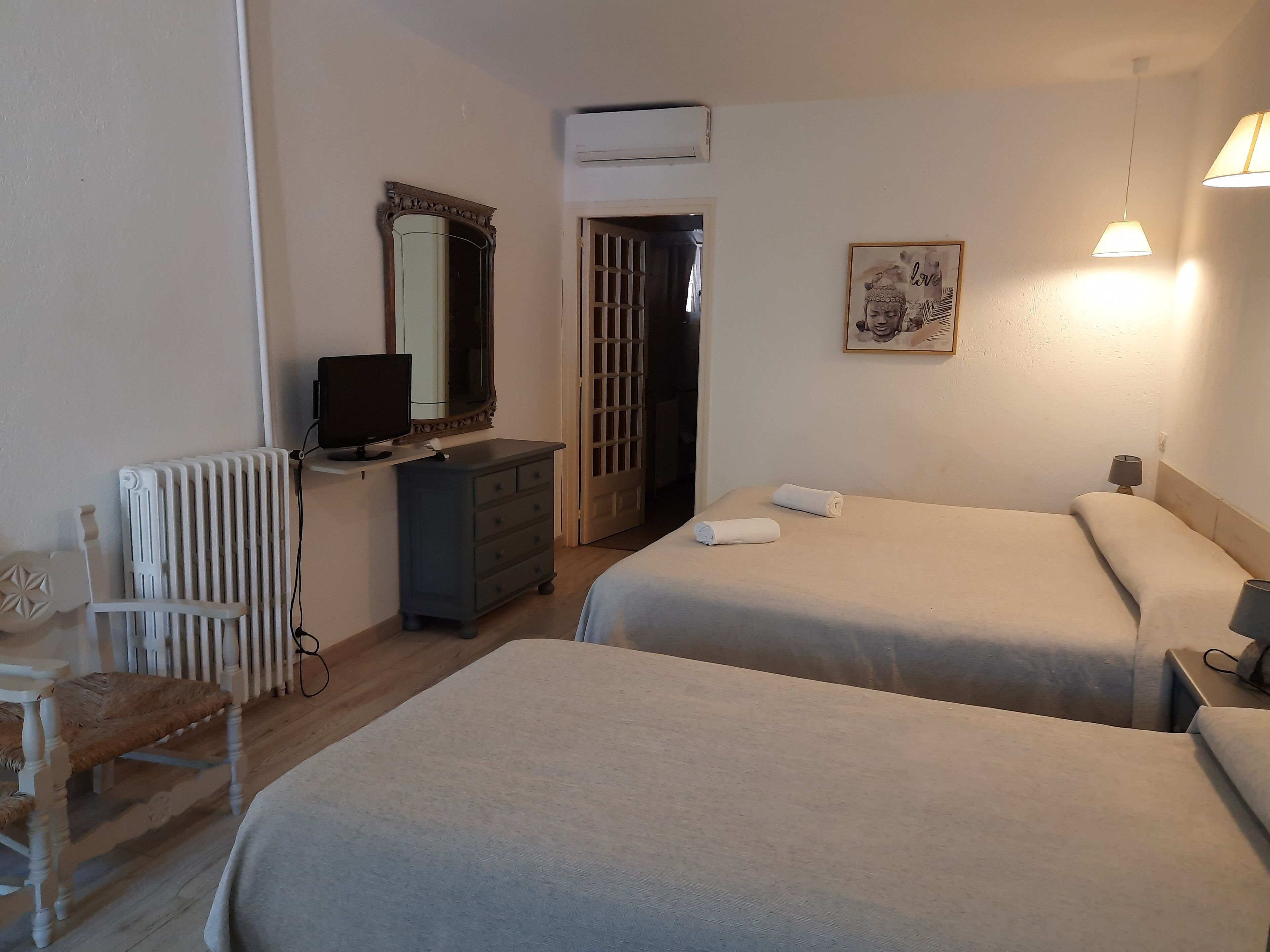 A hotel room with two beds, a dresser, a chair, a radiator, a television, and a painting on the wall.