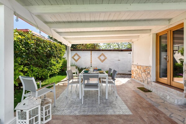 Une terrasse couverte avec une table dressée pour quatre personnes, entourée de chaises, et une petite table d’appoint avec des lanternes.