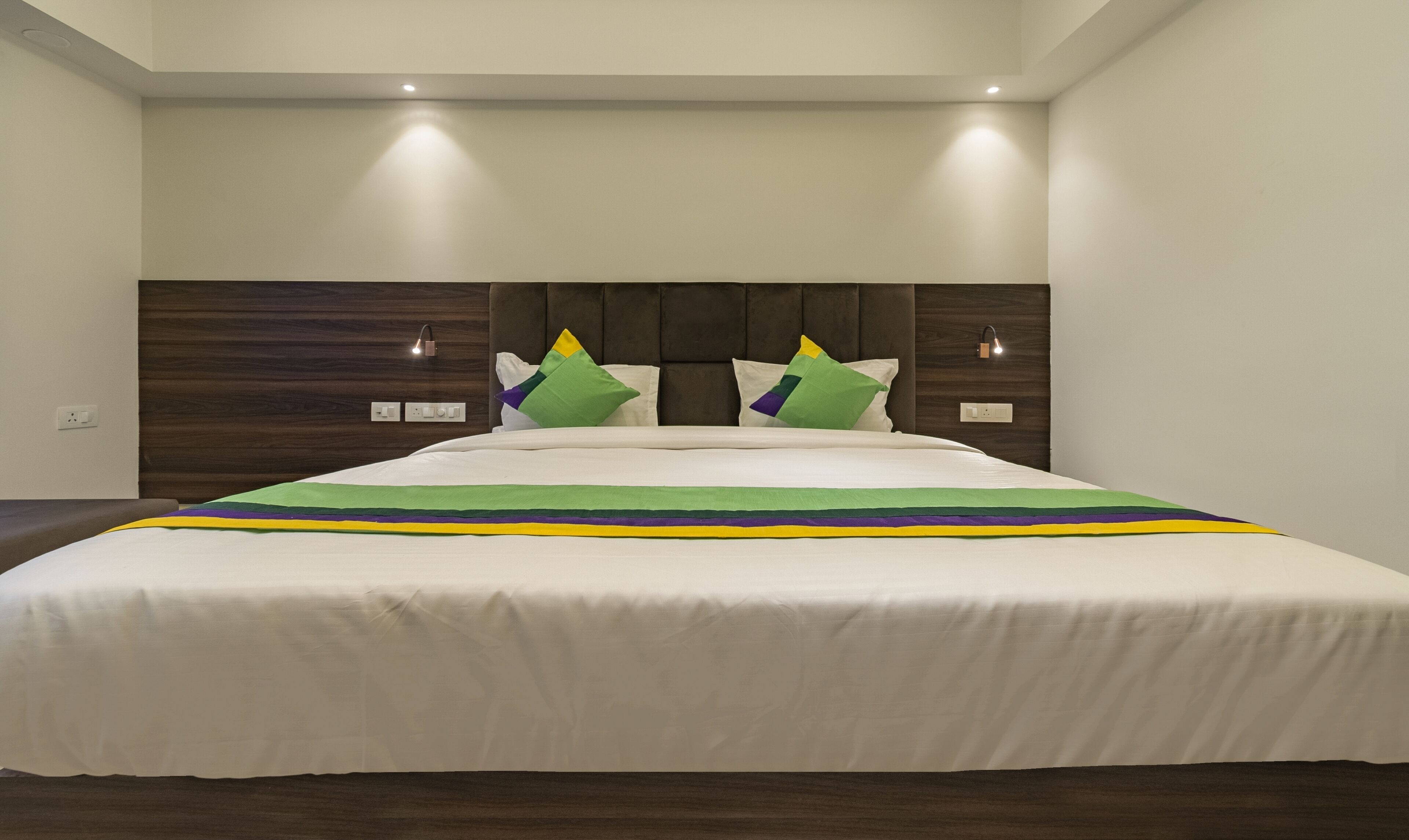 A modern hotel room with a large bed, dark wood headboard, and two bedside lamps.