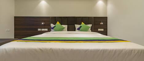 A modern hotel room with a large bed, dark wood headboard, and two bedside lamps.