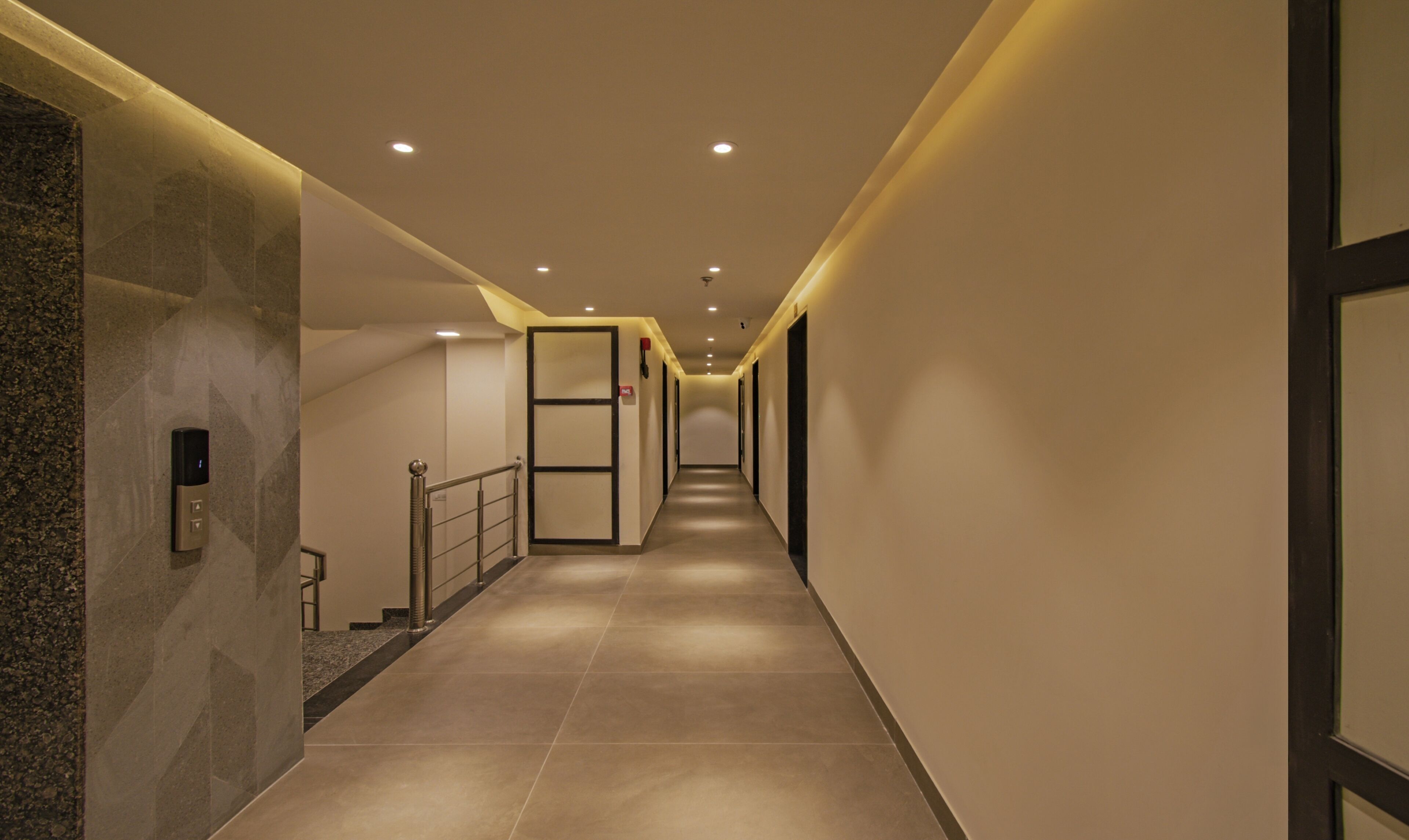 A long, well-lit hallway with a modern design, featuring a marble wall on one side and a glass door on the other.